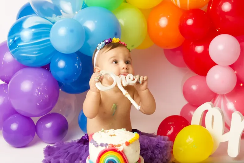 Bambina che assaggia la torta fra i palloncini arcobaleno