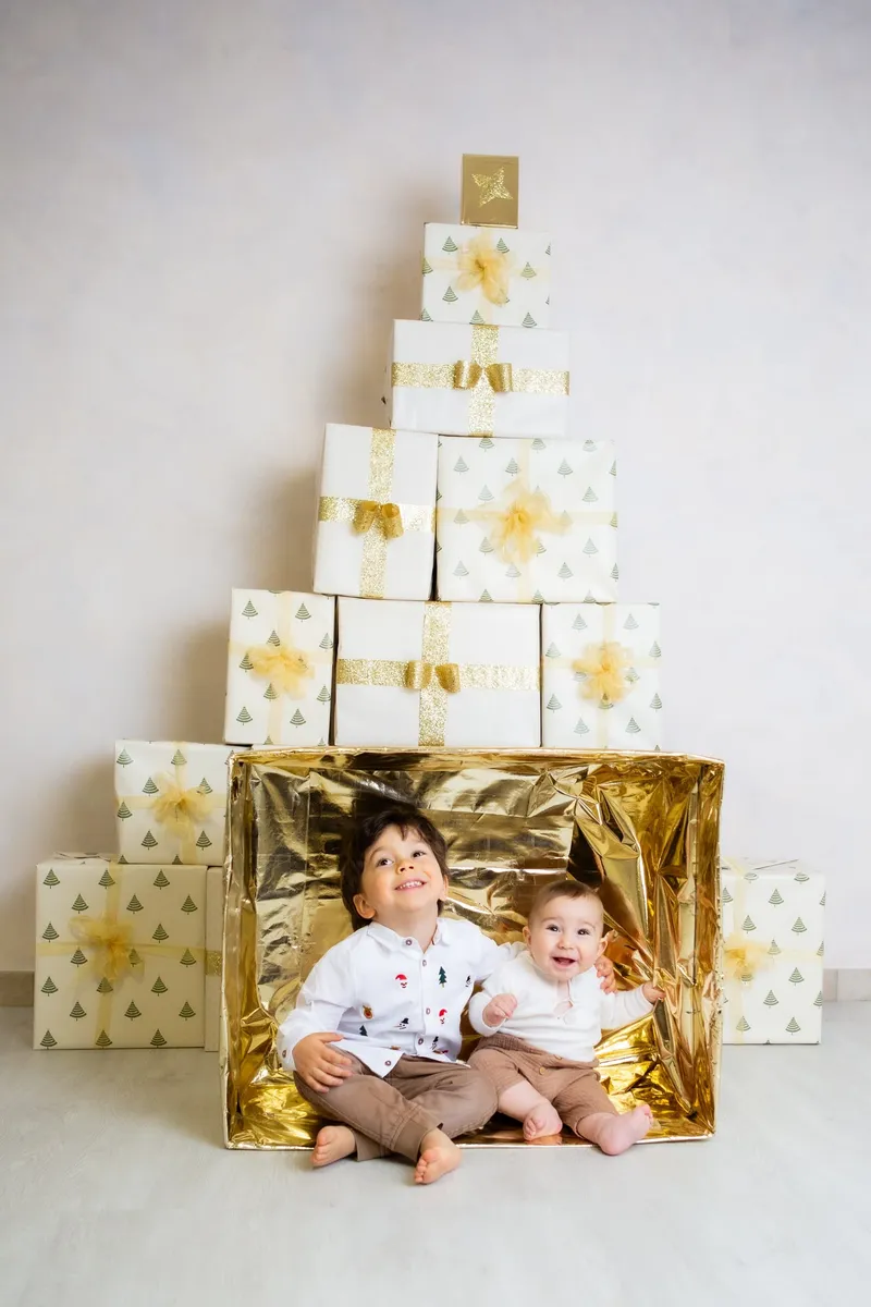 Due bambini in una scatola dorata sotto un albero di pacchi
