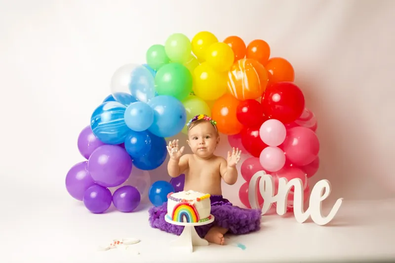 Bambino con torta arcobaleno e palloncini colorati