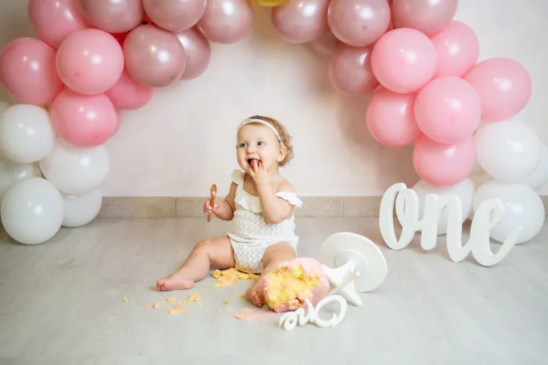 Bambina con la torta sotto un arco di palloncini rosa