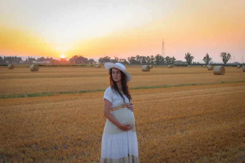 Donna incinta con il cappello in un campo al tramonto