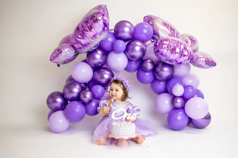 Bambina in viola sotto un arco di palloncini viola