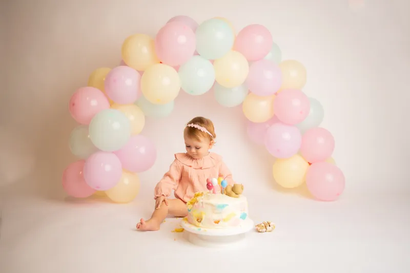 Bambina con la torta sotto un arco di palloncini pastello