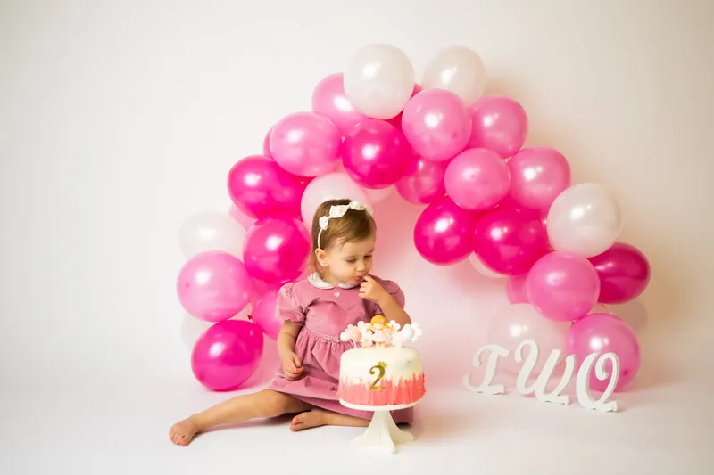 Bambina con la torta dei due anni e palloncini fucsia