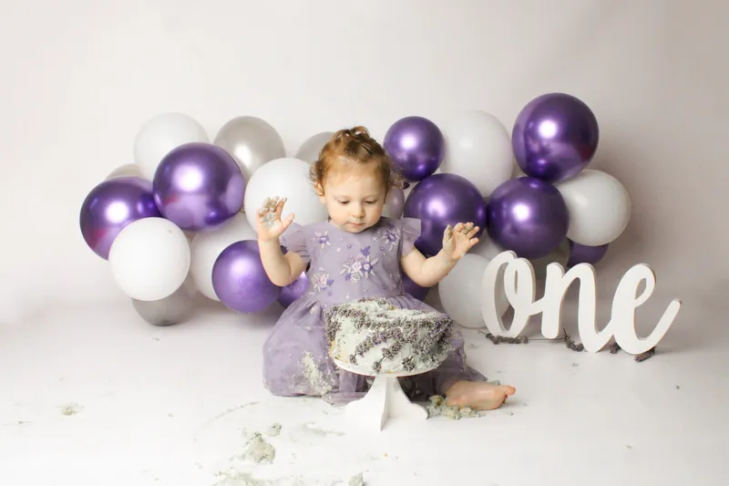 Bambina in viola con torta e palloncini viola