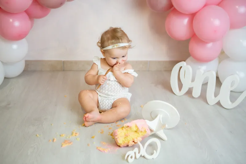 Bambina che mangia la torta fra palloncini rosa