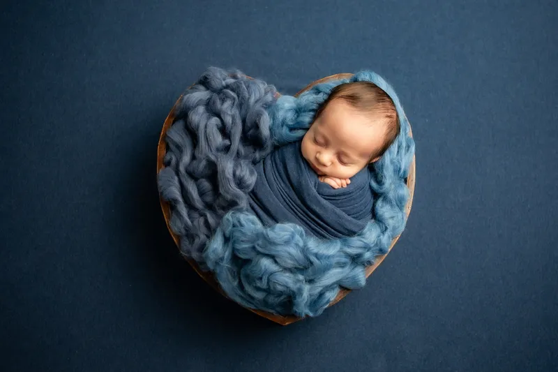 Neonato in un cesto a cuore su fondo blu