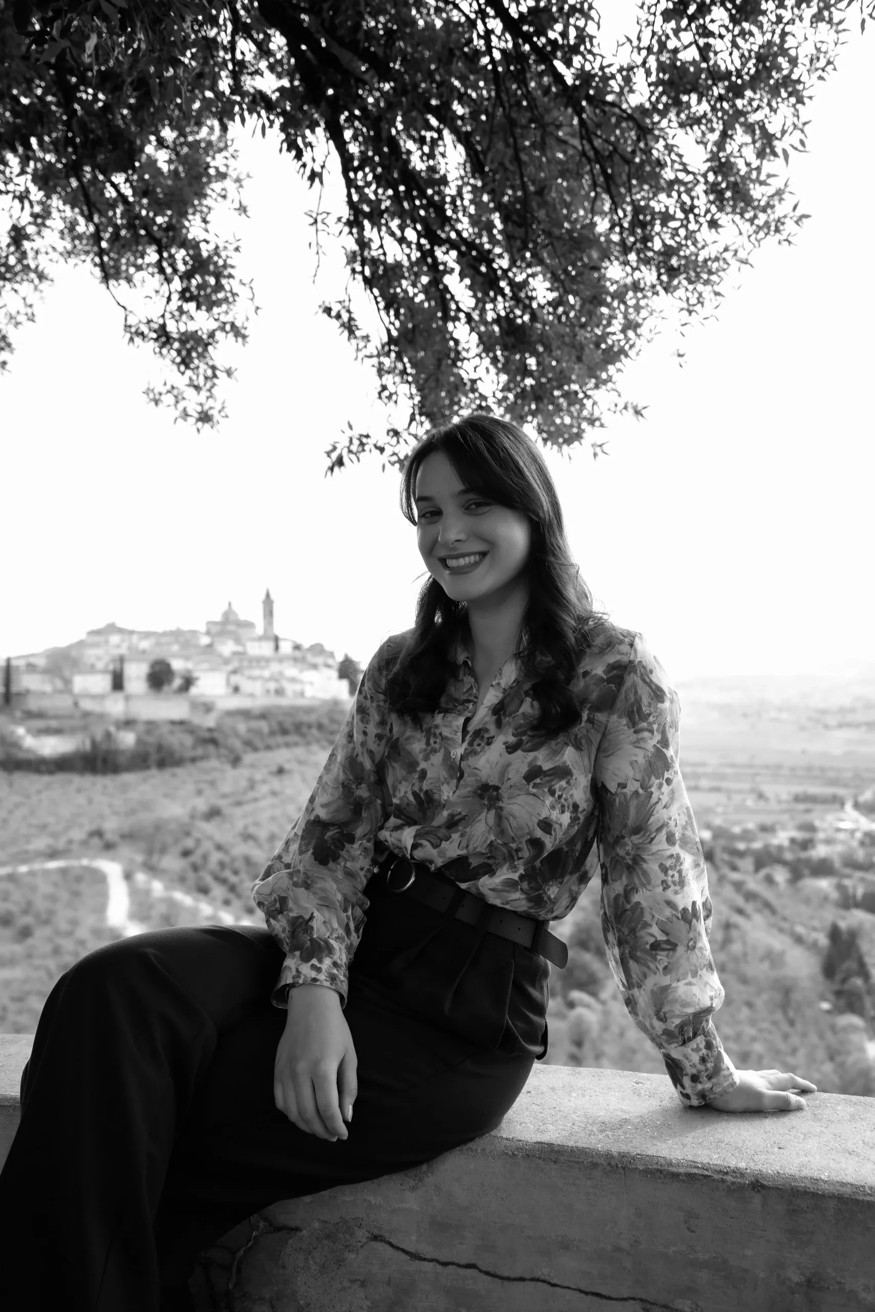 Ritratto in bianco e nero di Chiara all’aperto, con la campagna umbra e il borgo di Trevi sullo sfondo